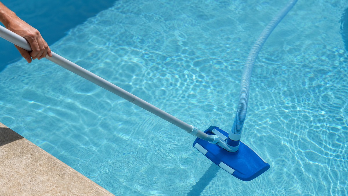 Limpa-fundos manual com cabeça e vara a aspirar o fundo de uma piscina residencial